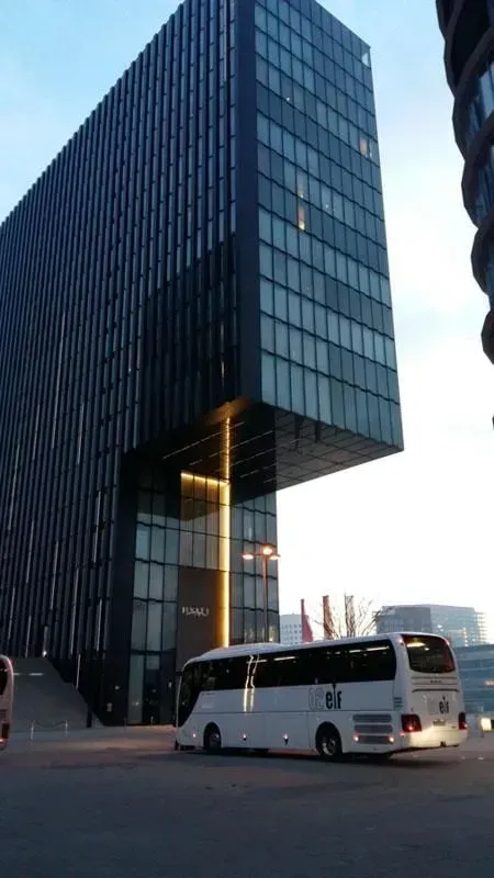 Ein weißer Bus steht vor einem hohen Gebäude 02elf Travel GmbH & Co KG
