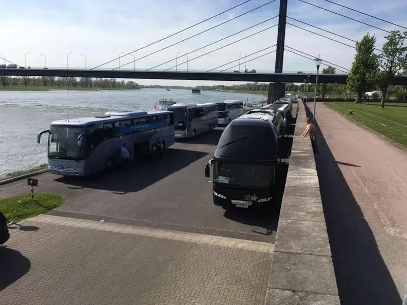 Eine Reihe von Bussen parkt neben einem Fluss, 02elf Travel GmbH & Co KG