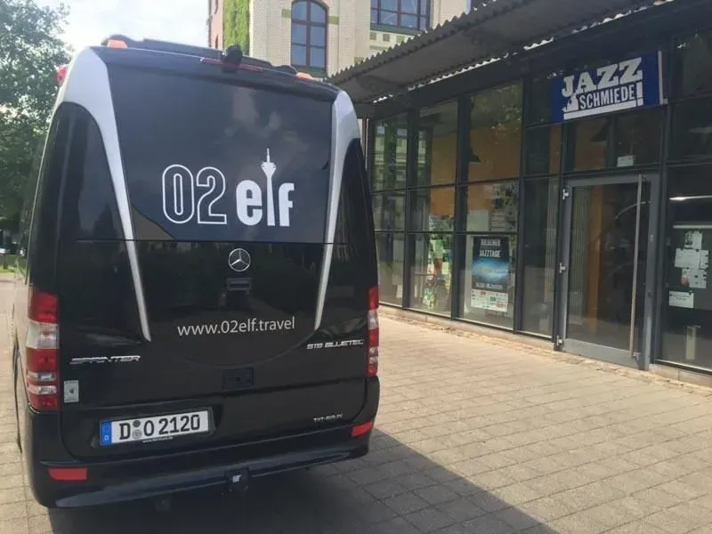 Ein schwarzer Lieferwagen mit 02 Elf auf der Rückseite steht vor einem Gebäude, 02elf Travel GmbH & Co KG