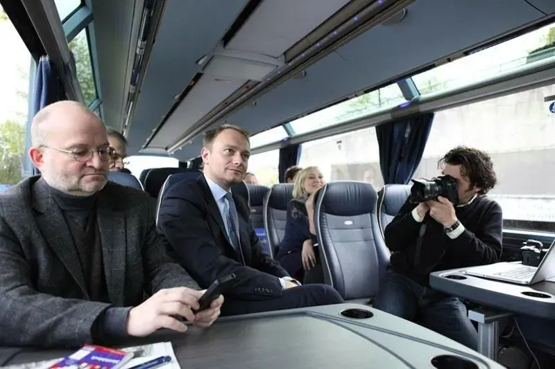 Ein Mann macht ein Foto von einer Gruppe von Menschen in einem Bus, darunter Christian Lindner, 02elf Travel GmbH & Co KG