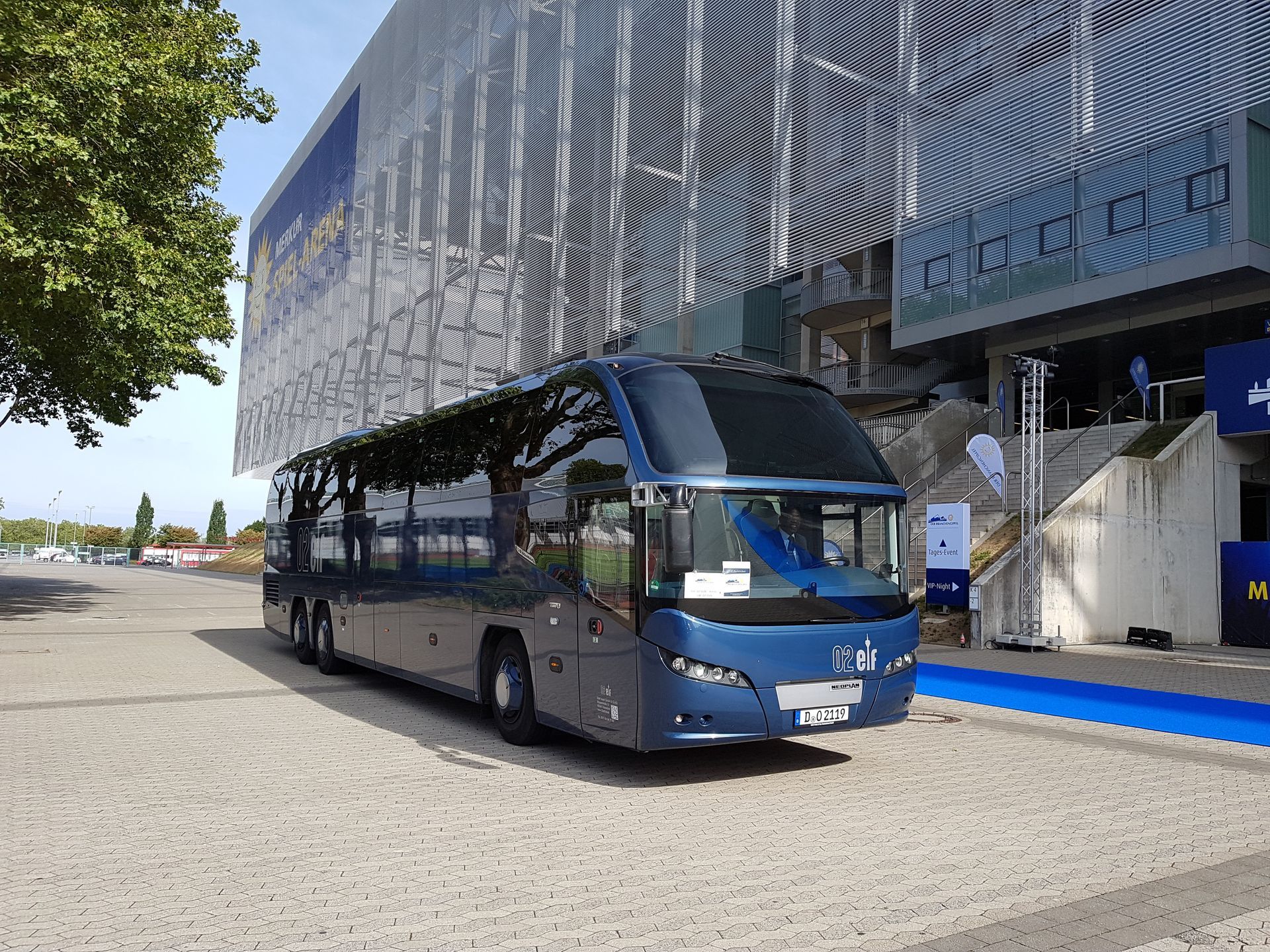 Ein blauer Reisebus parkt vor einem modernen Gebäude mit silberner Fassade.