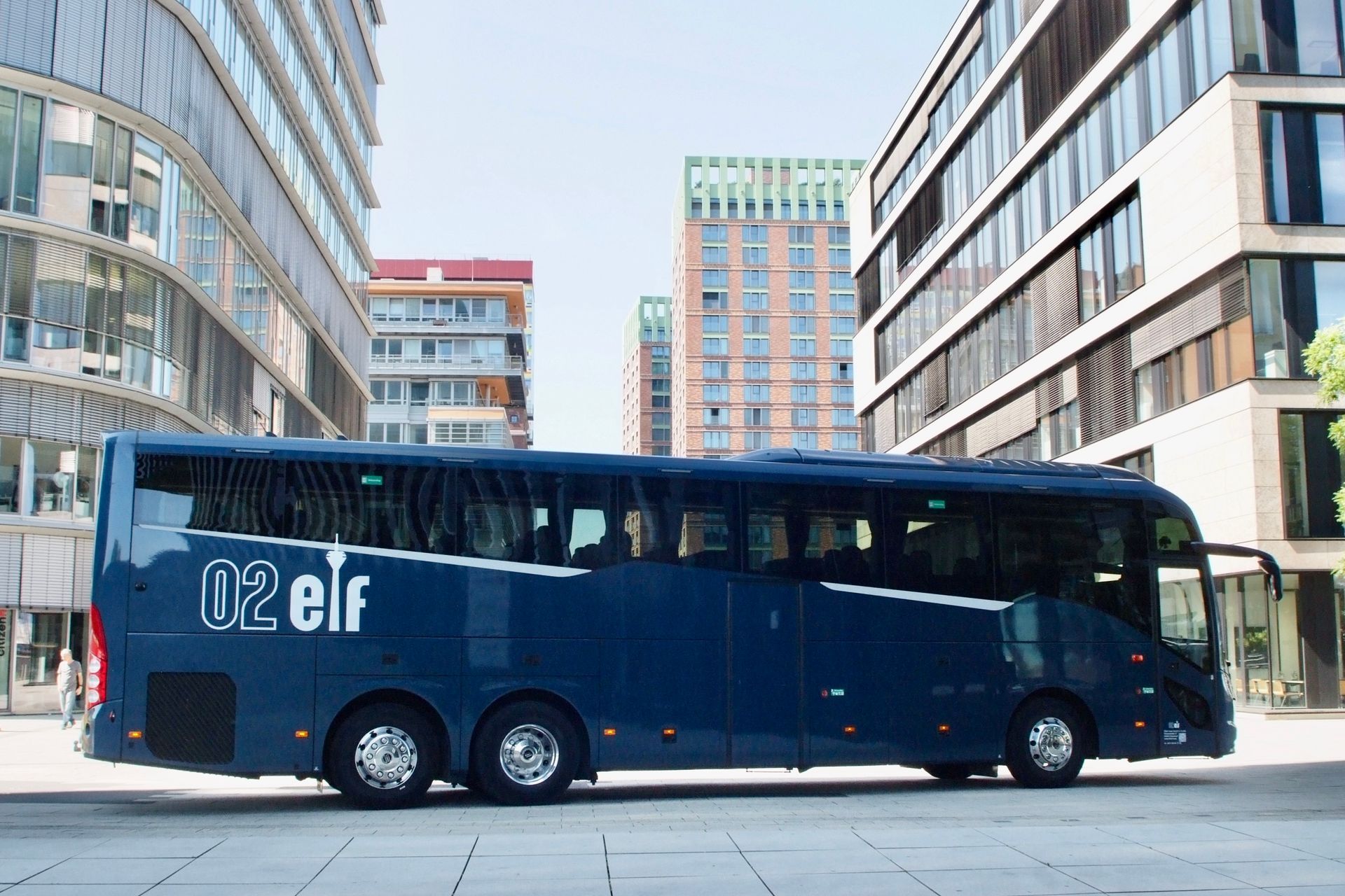 Dunkelblauer „Elfen“-Bus auf einer Stadtstraße zwischen modernen Bürogebäuden