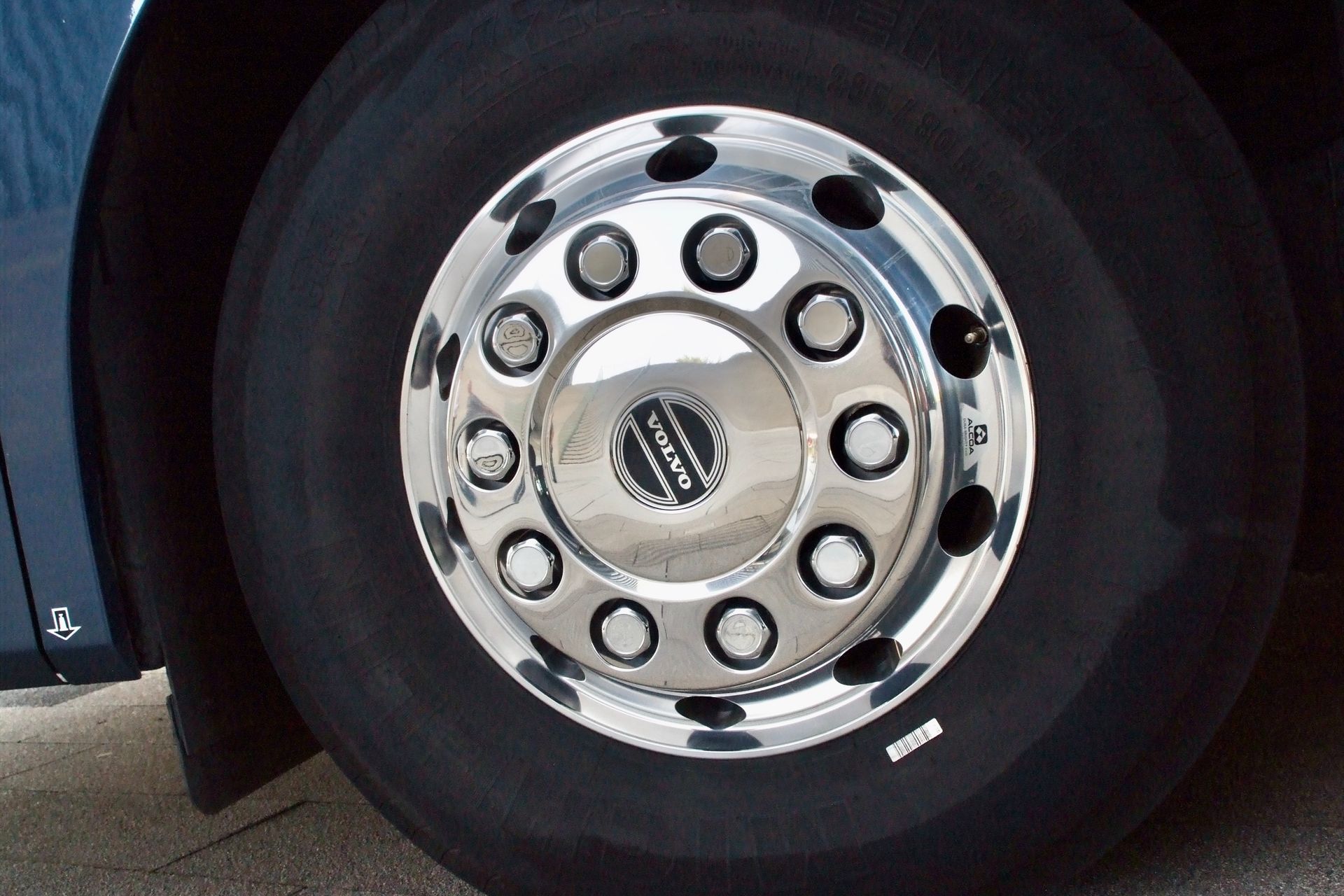 Nahaufnahme eines glänzenden verchromten LKW-Rads mit schwarzem Reifen auf dem Asphalt.