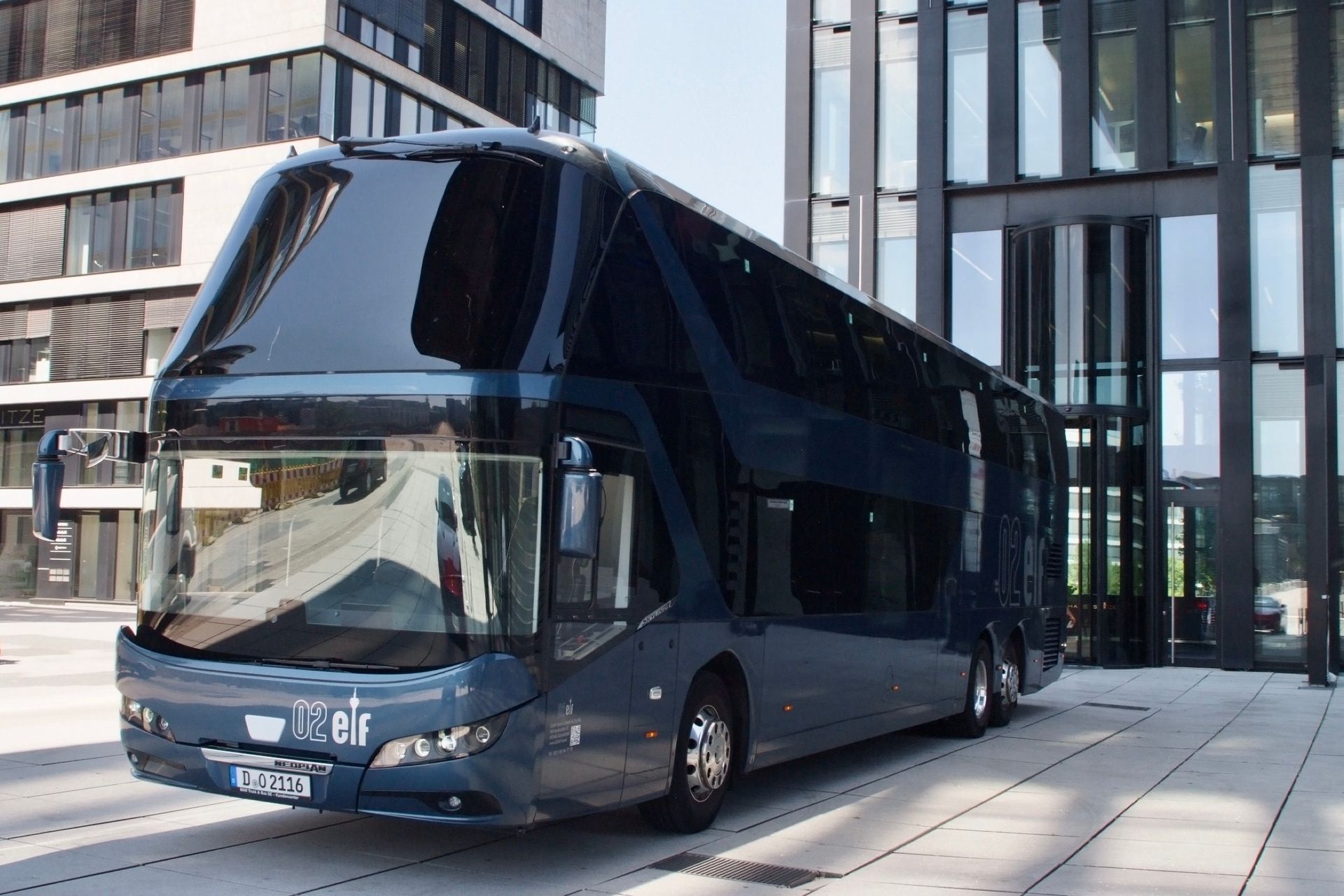 Ein dunkelblauer Doppeldeckerbus parkt vor einem modernen Glasgebäude