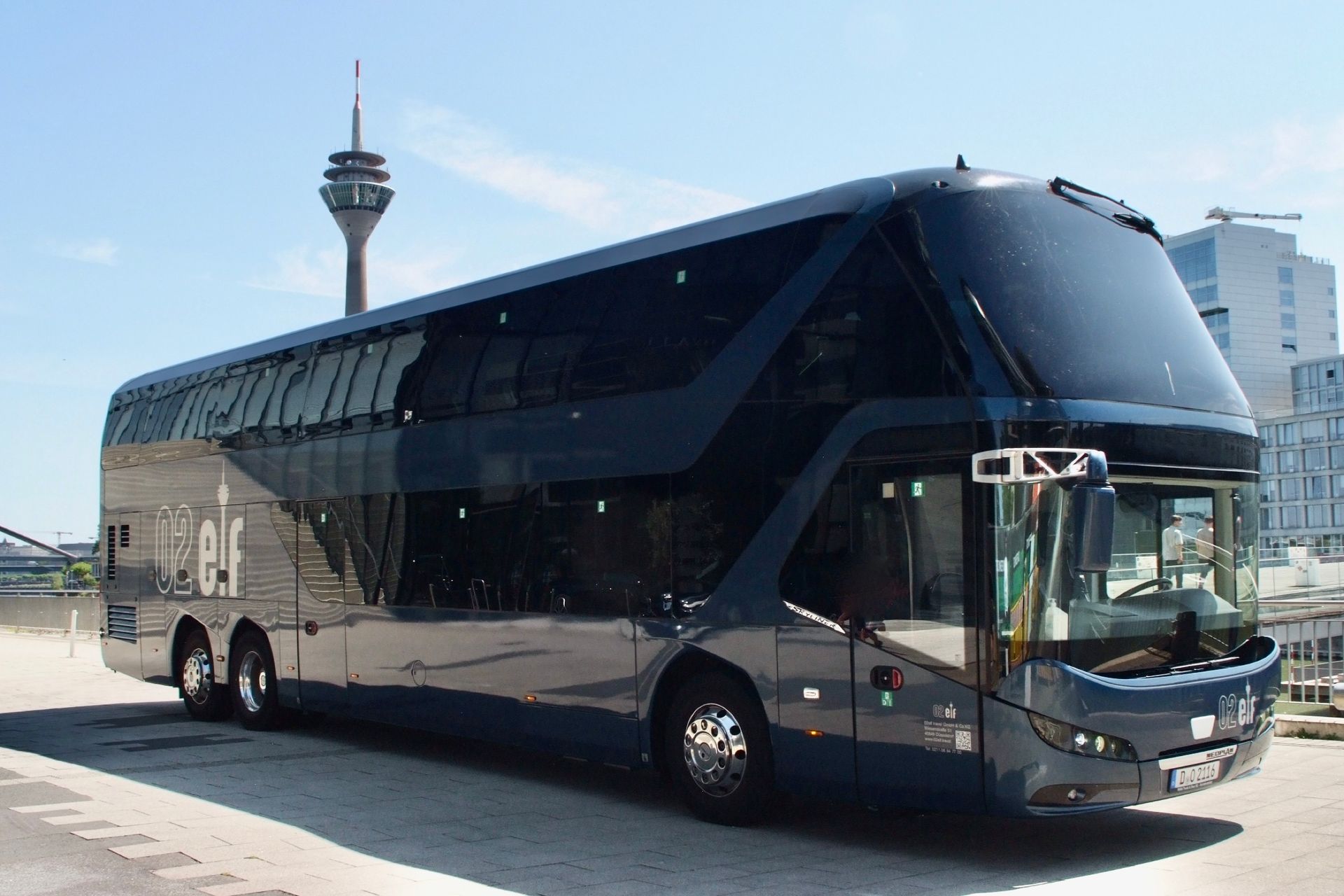 Ein schwarzer Doppeldeckerbus parkt im Freien, im Hintergrund ist ein Turm zu sehen.