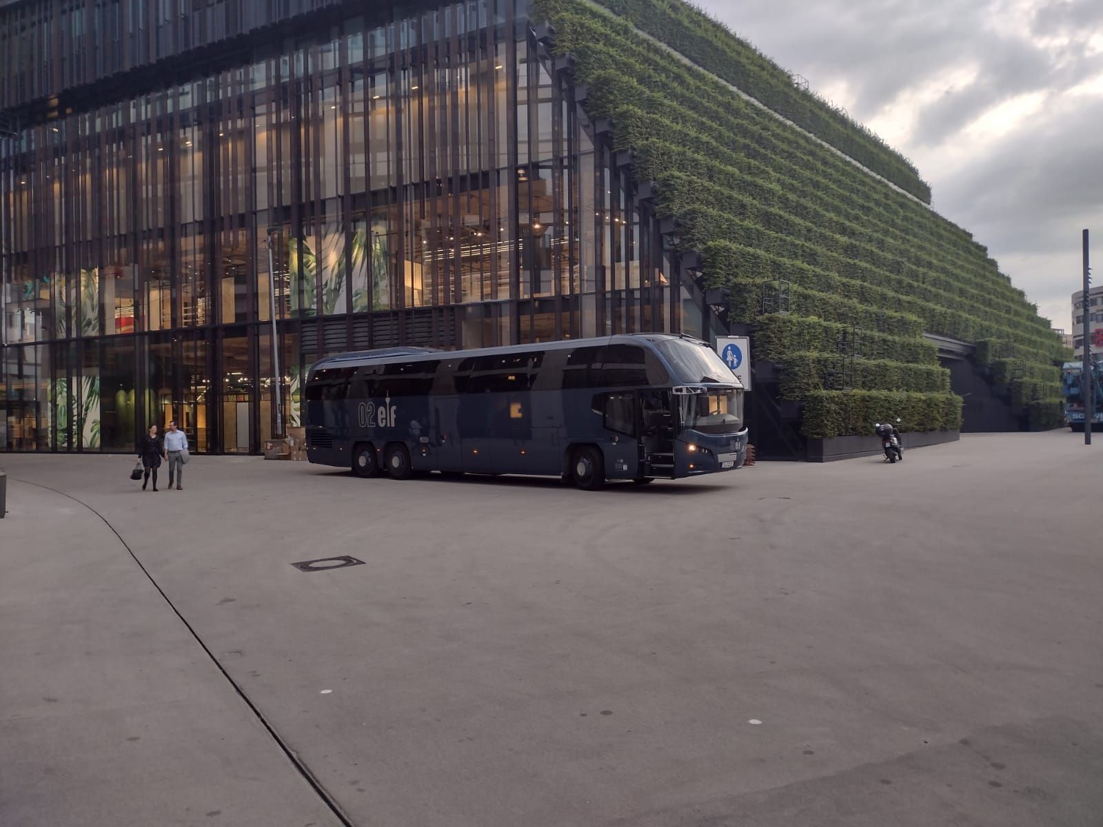 Modernes Glasgebäude mit einem davor auf einem großen Platz geparkten Bus