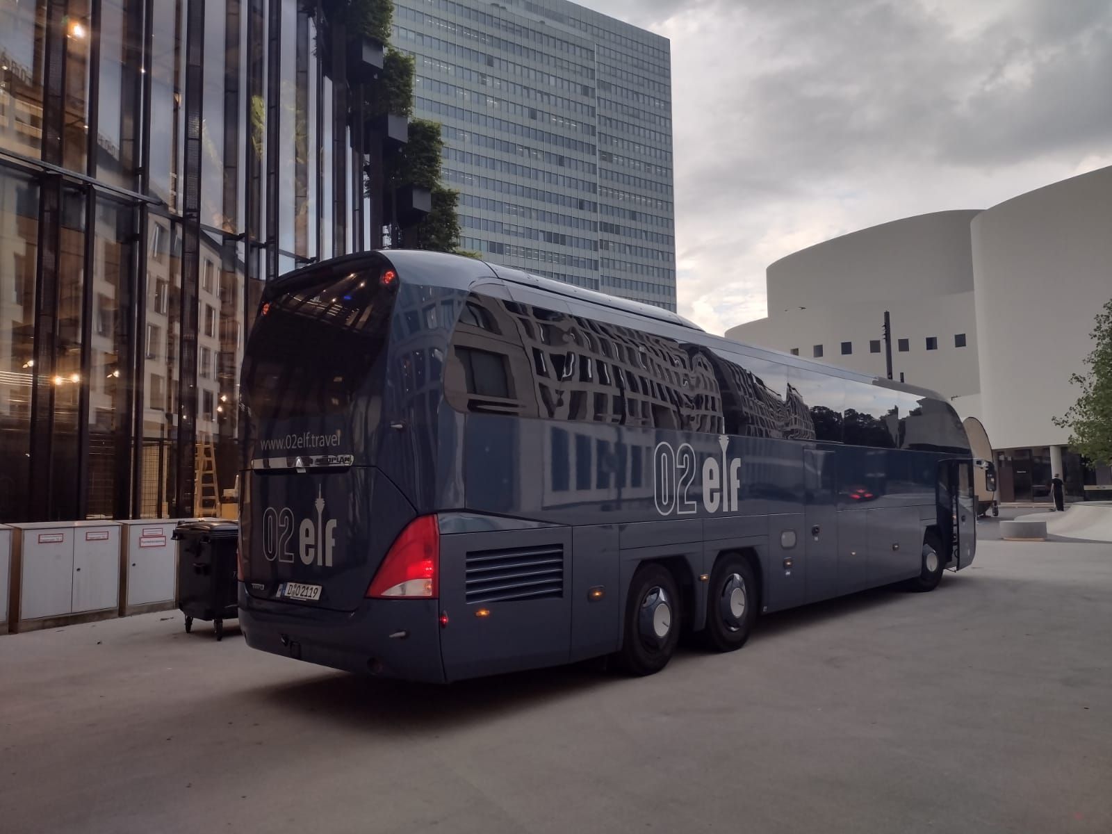 Ein dunkelblauer Reisebus parkt neben modernen Gebäuden in einer Stadtstraße.