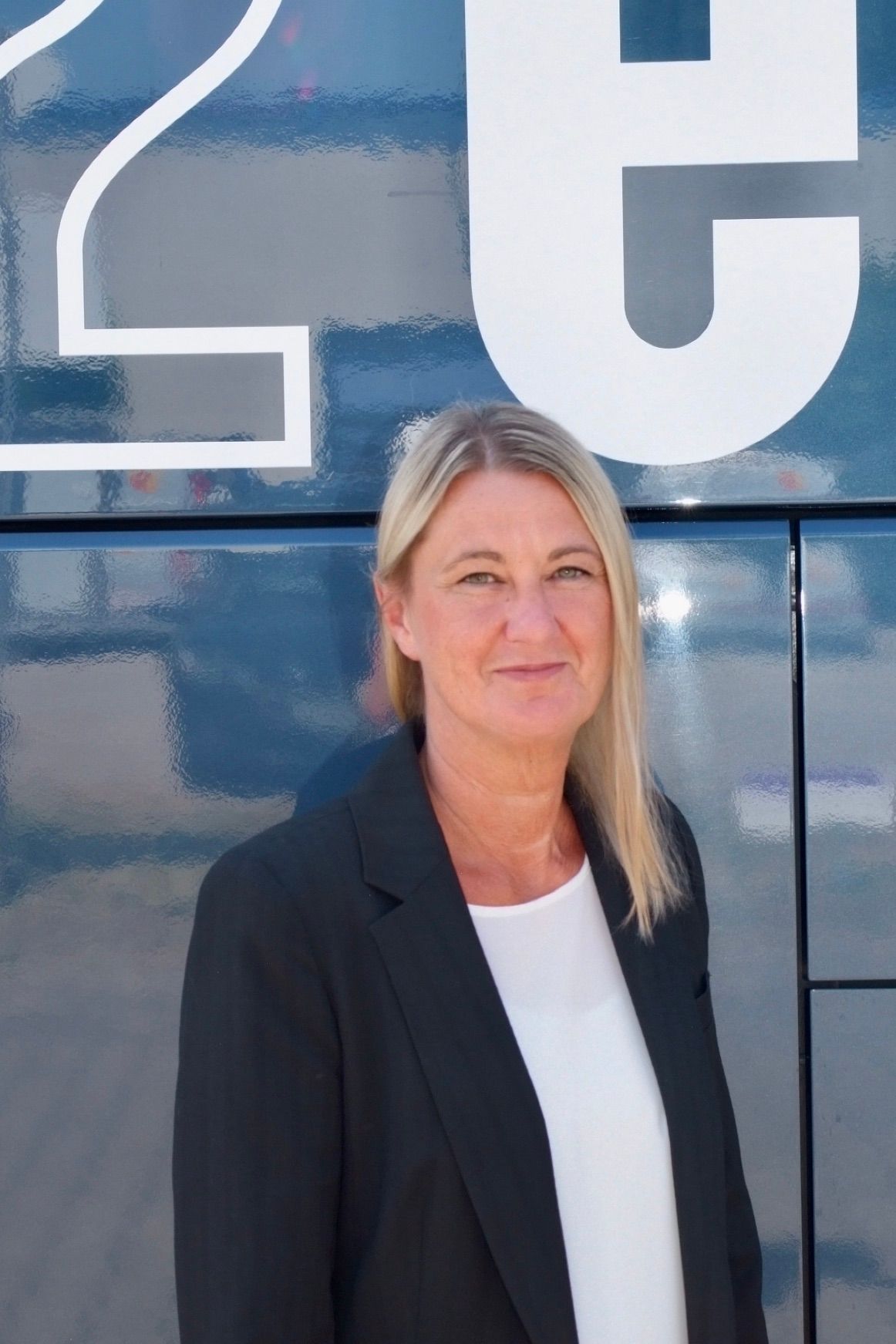 Eine Frau in einem blauen Hemd steht vor einem weißen Hintergrund.
