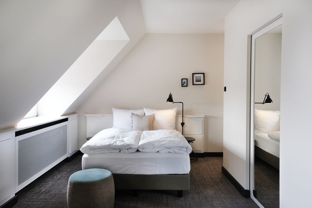 Studio L-Apartment - Zu sehen sind ein Doppelbett, ein Hocker, eine Stehlampe und ein großes Fenster