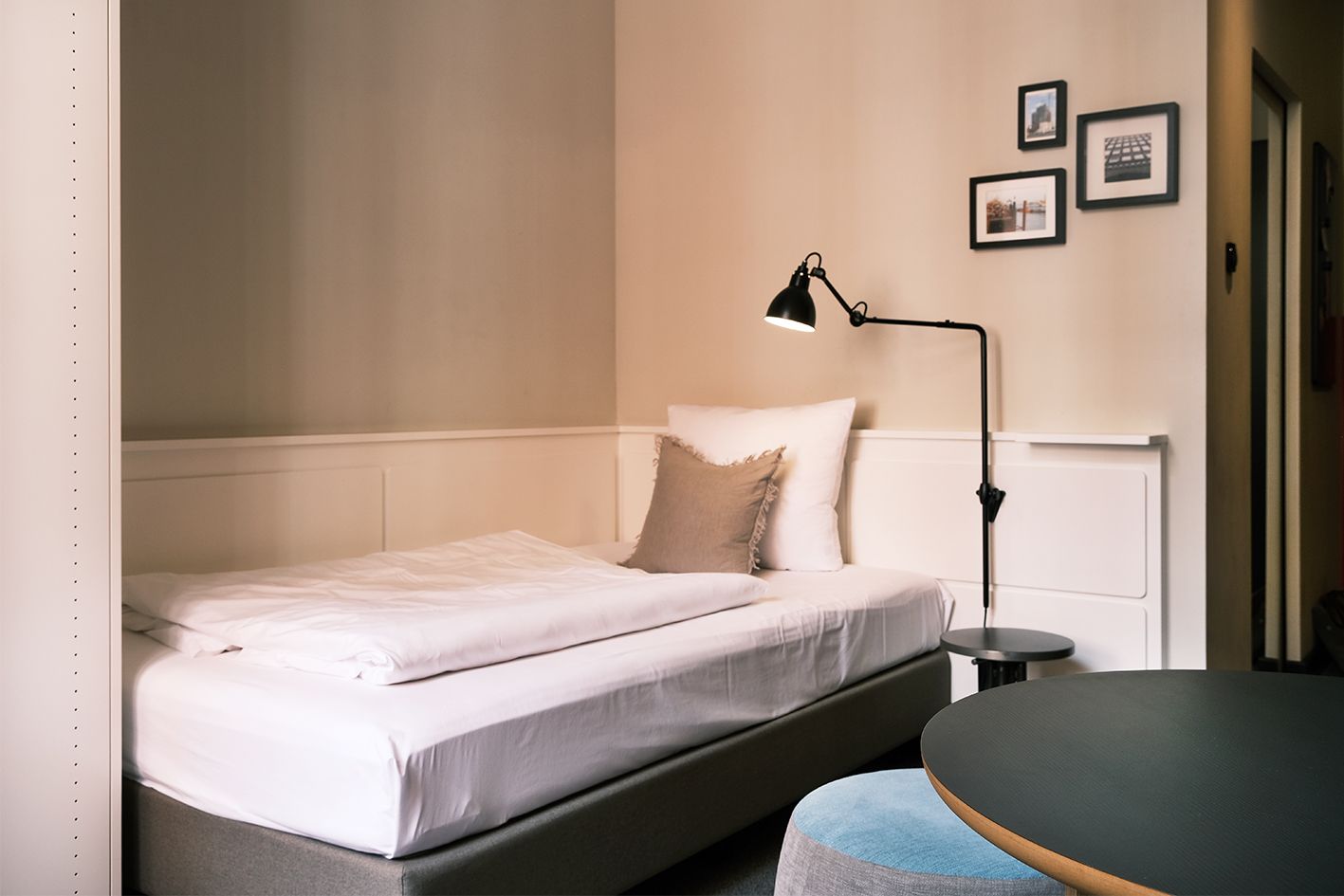 Ein Schlafzimmer mit Einzelbett, Tisch, Lampe und Bildern an der Wand.