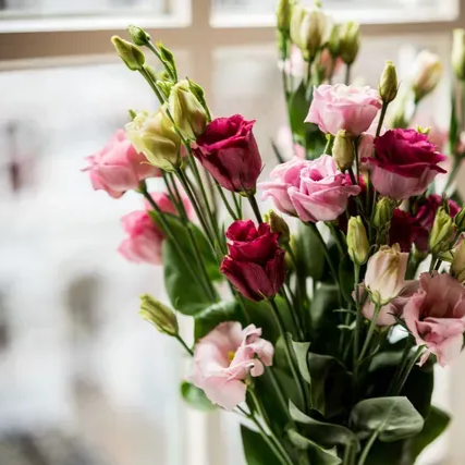 Eine Frau sitzt an einem Schreibtisch vor einem Fenster und arbeitet am Laptop. Hinter ihr steht ein großer Strauß Blumen.