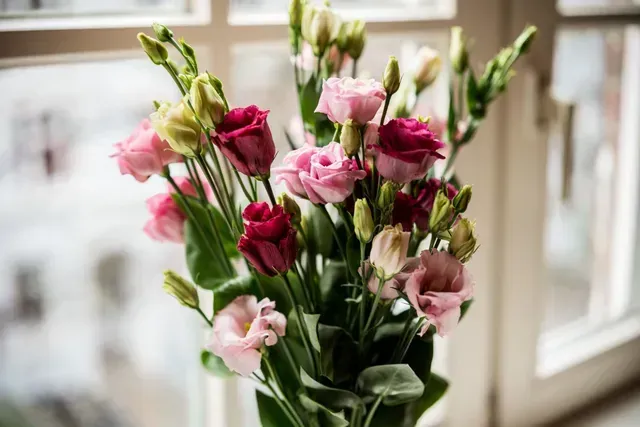 Vor einem Fenster steht eine Vase mit rosa und roten Blumen.