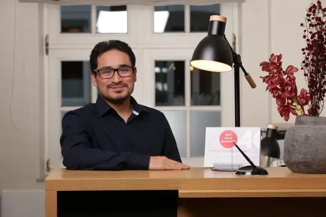 Ein Mann mit Brille sitzt an einem Schreibtisch mit einer Lampe.