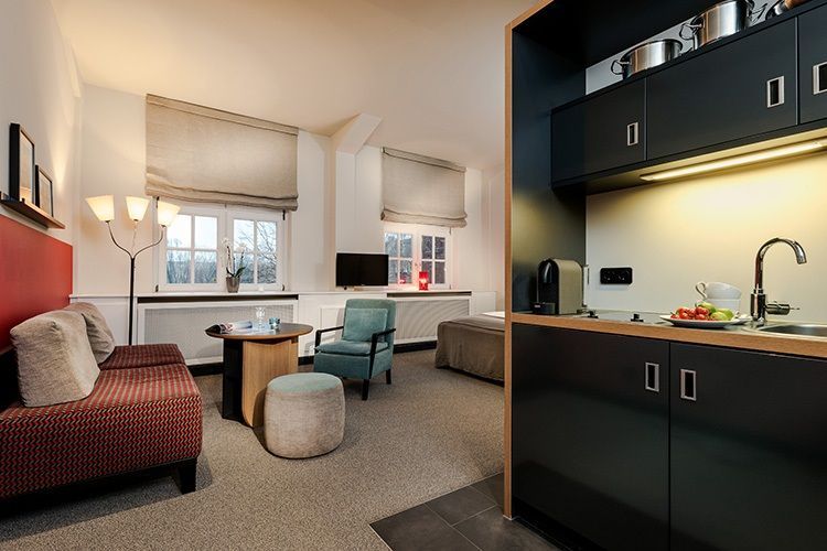 Ein offener Raum mit Küchenzeile, mehreren Sitzgelegenheiten und einem Bett