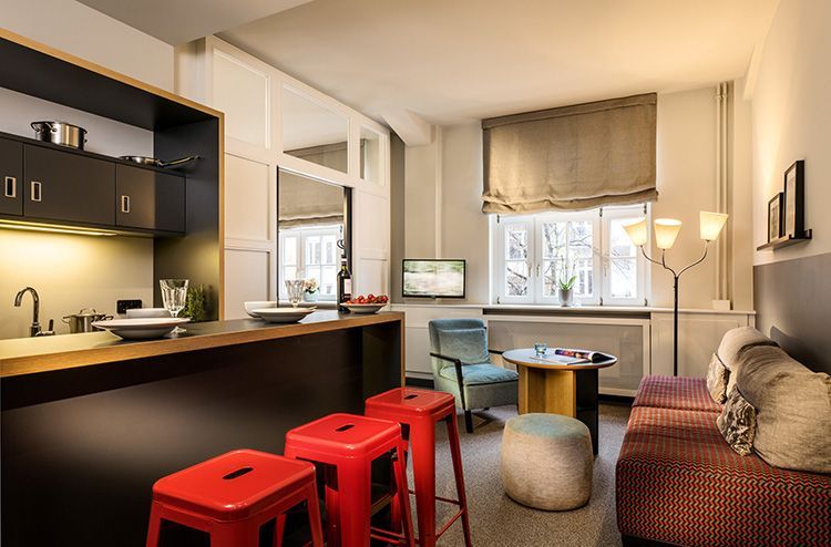 Ein Wohnzimmer mit roten Hockern, einer Couch, einem Tisch und einer Küche.