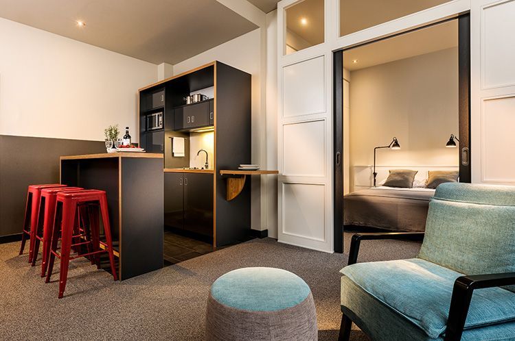Junior Suite des Apartment040. Zu sehen ist die Kitchenette mit 3 Sitzhockern, der Schlafbereich und ein blauer Sessel