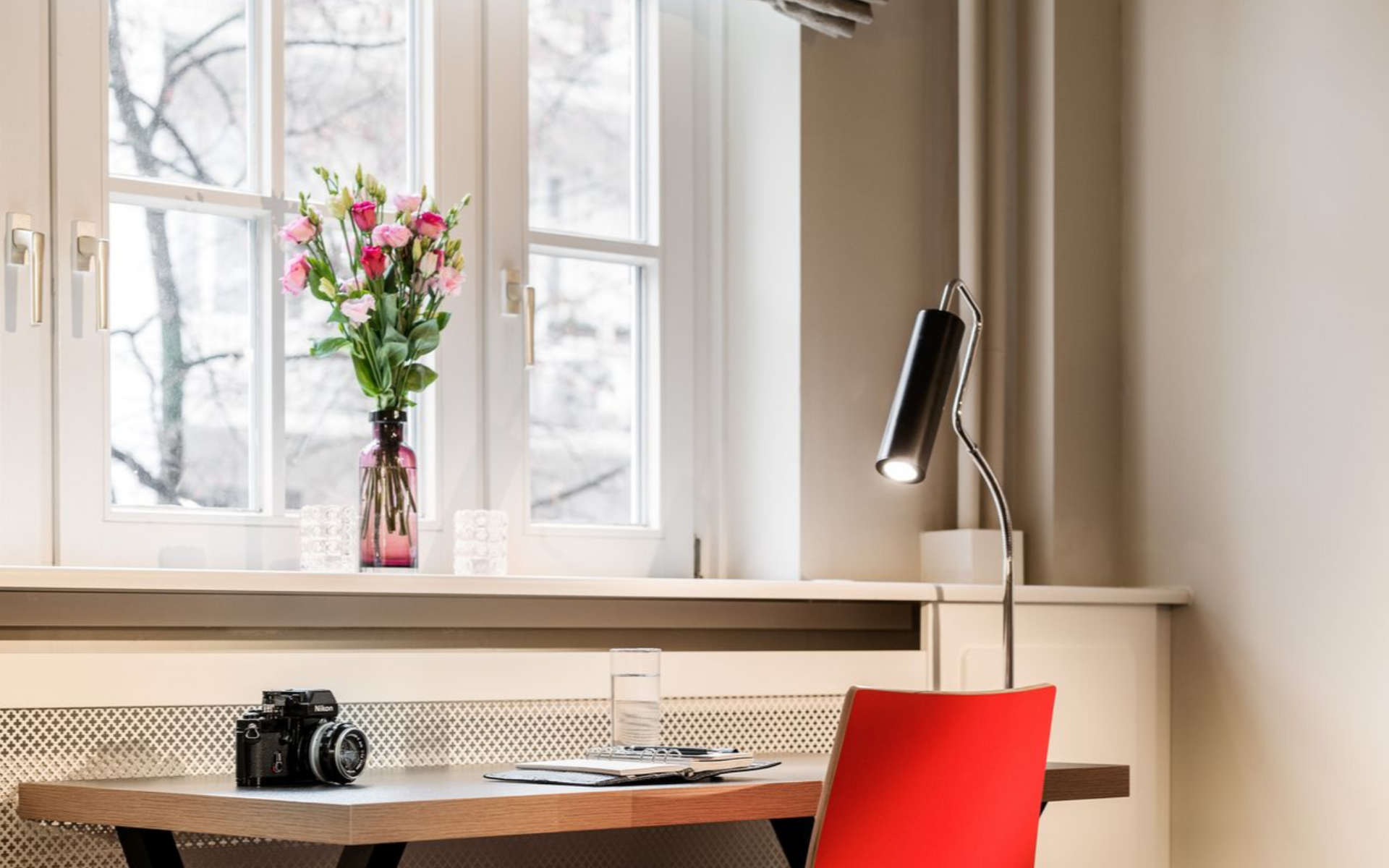 Eine Frau sitzt an einem Schreibtisch vor einem Fenster und arbeitet am Laptop. Hinter ihr steht ein großer Strauß Blumen.