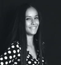 Una mujer con cabello largo y oscuro, vestida con un top de lunares, sonríe a la cámara.