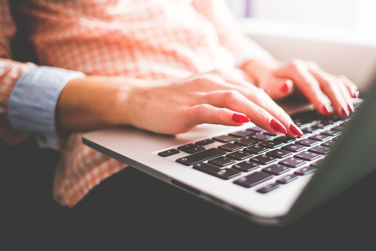 Una mujer con uñas rojas está escribiendo en una computadora portátil.