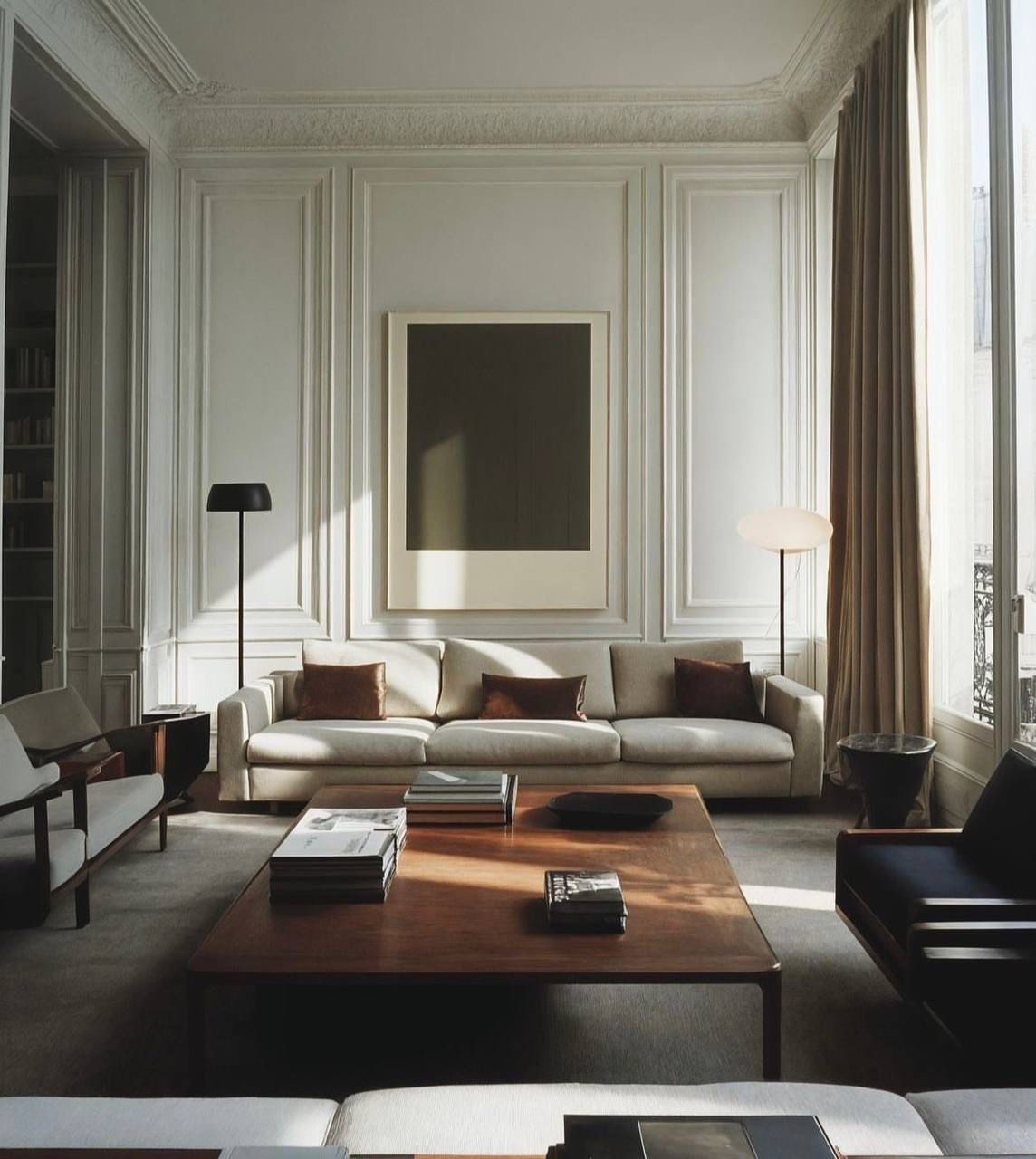 Sala de estar con paredes beige, un sofá moderno, obras de arte de gran tamaño y lámparas de pie.