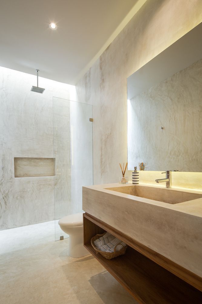 Baño moderno con lavabo y ducha de piedra, tonos neutros e iluminación empotrada.
