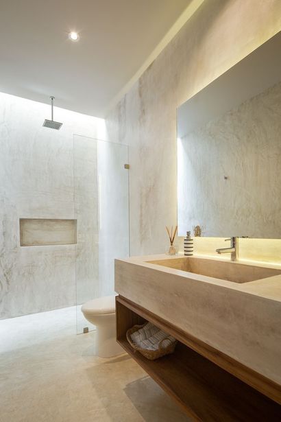 Baño moderno con lavabo y ducha de piedra, tonos neutros e iluminación empotrada.