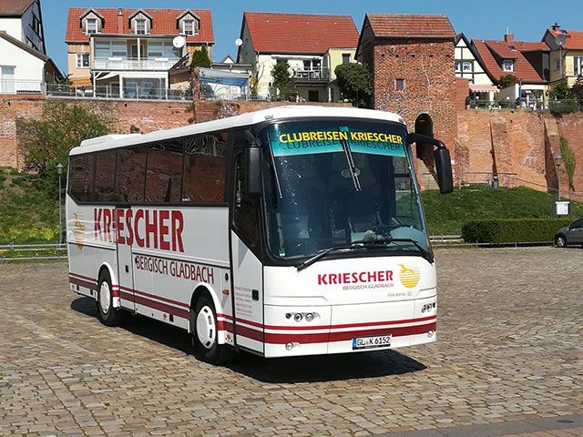 Ein weiß-roter Bus parkt vor einer Backsteinmauer.