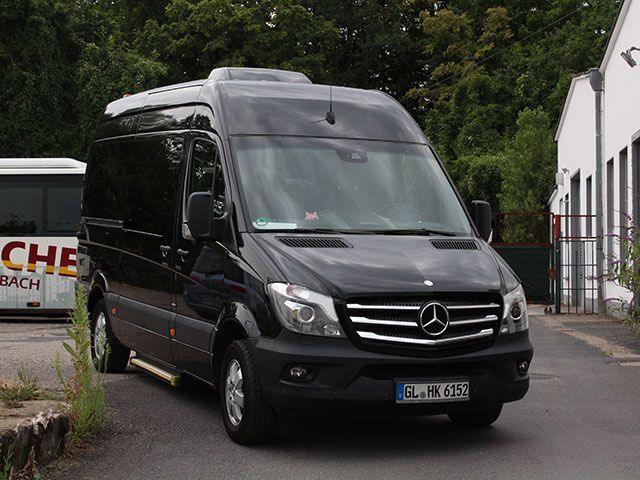 Ein schwarzer Mercedes-Van steht vor einem Gebäude.