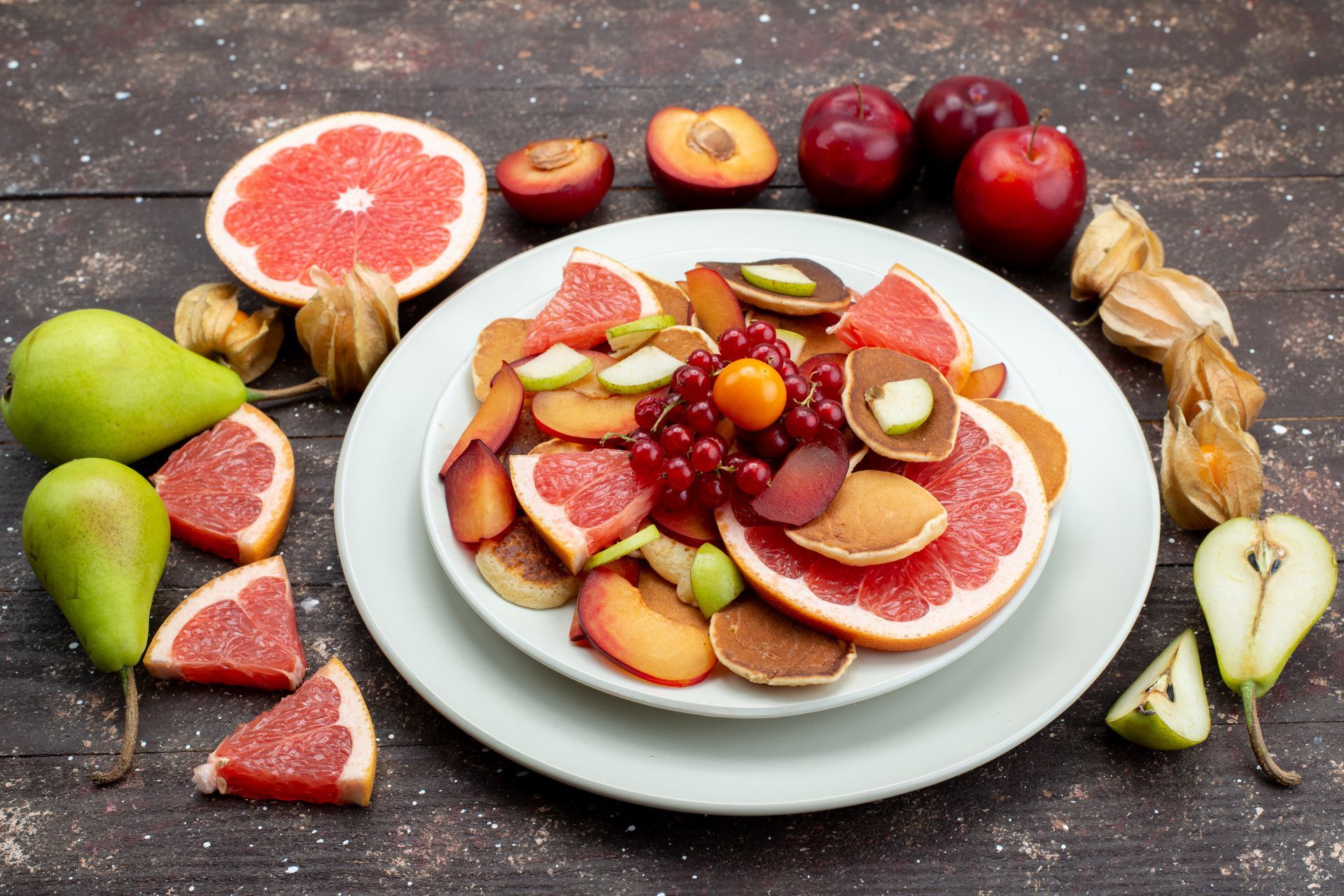 A white plate topped with sliced fruit and pancakes on a wooden table.