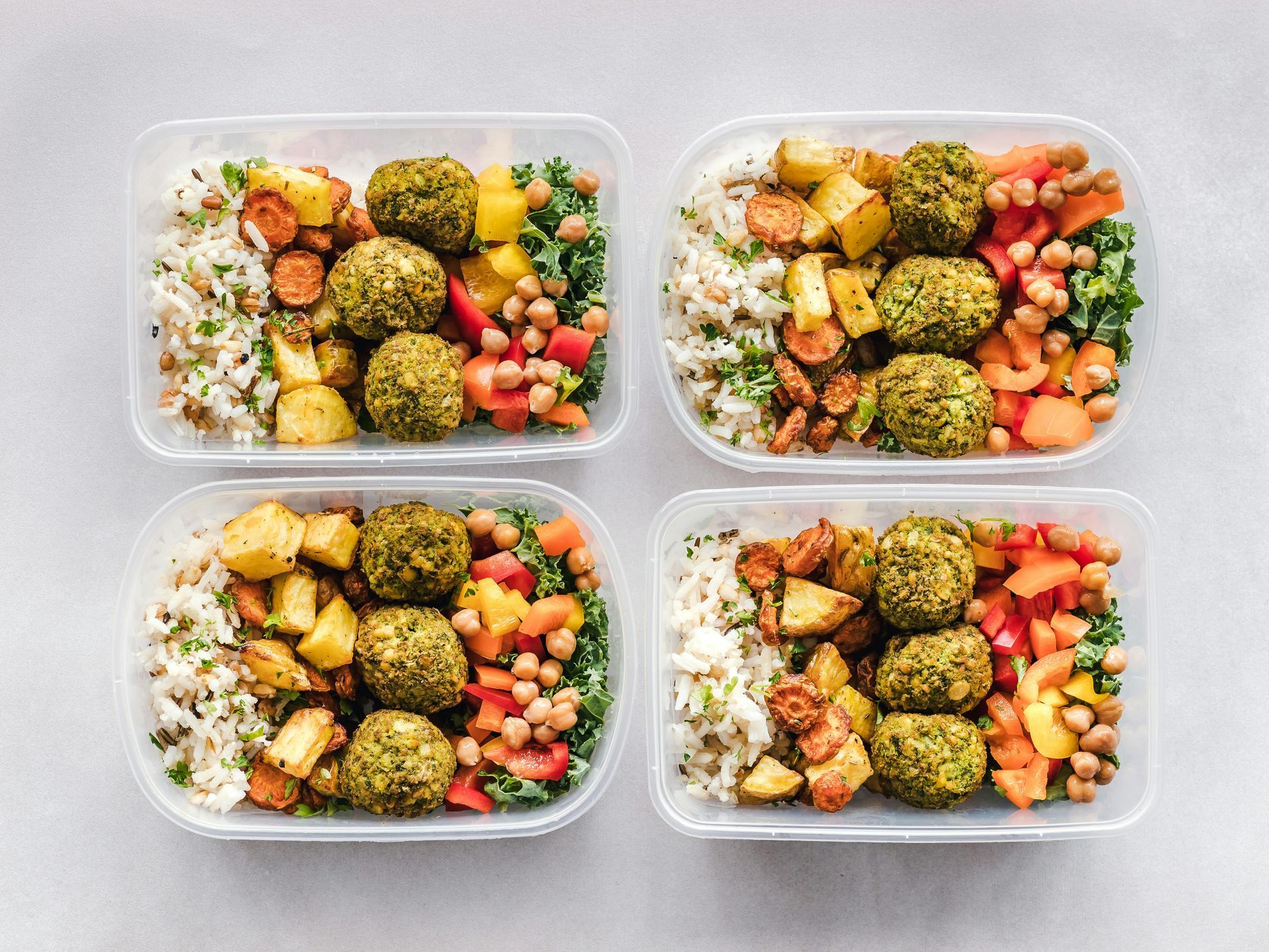 Four plastic containers filled with different types of food on a table.