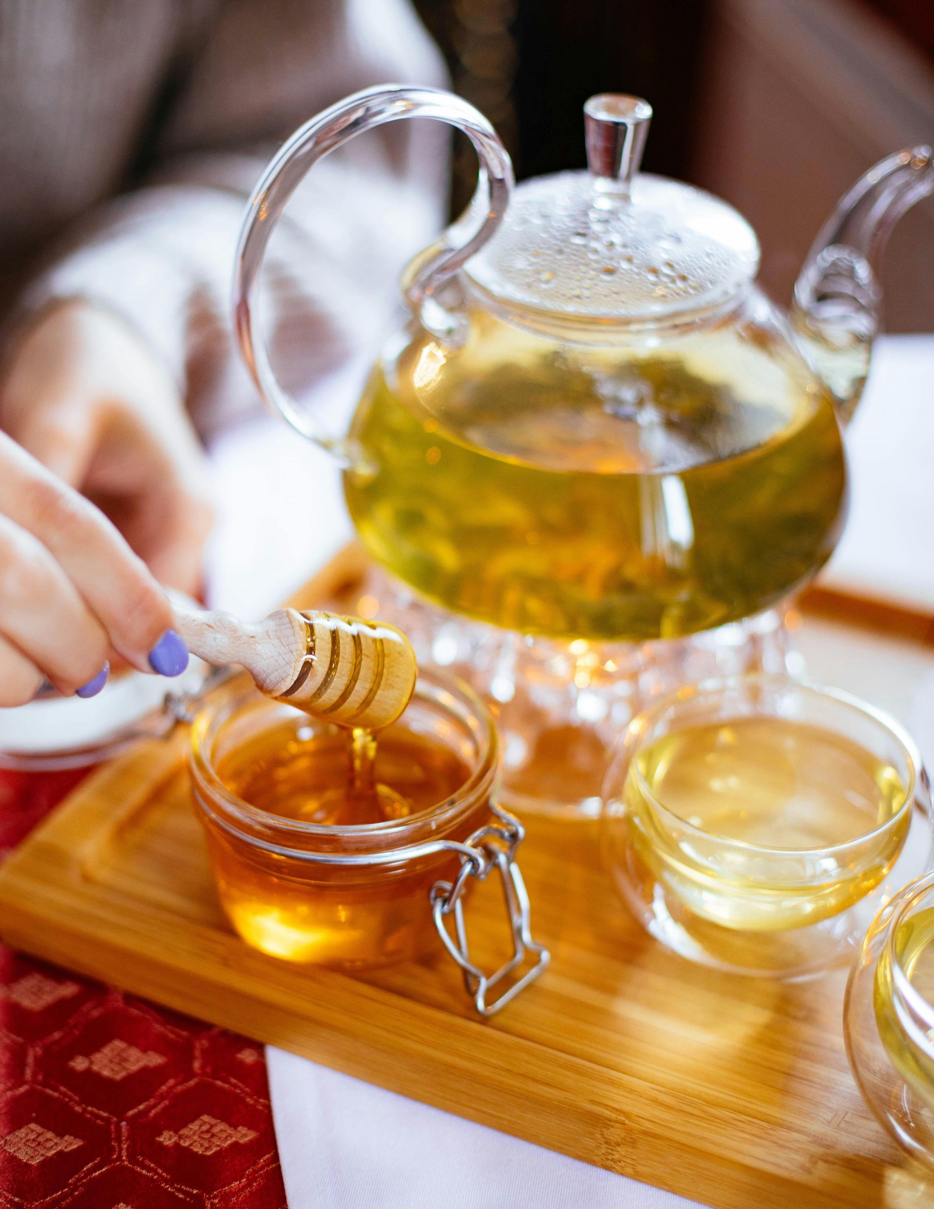 A woman is pouring honey into a jar of tea.