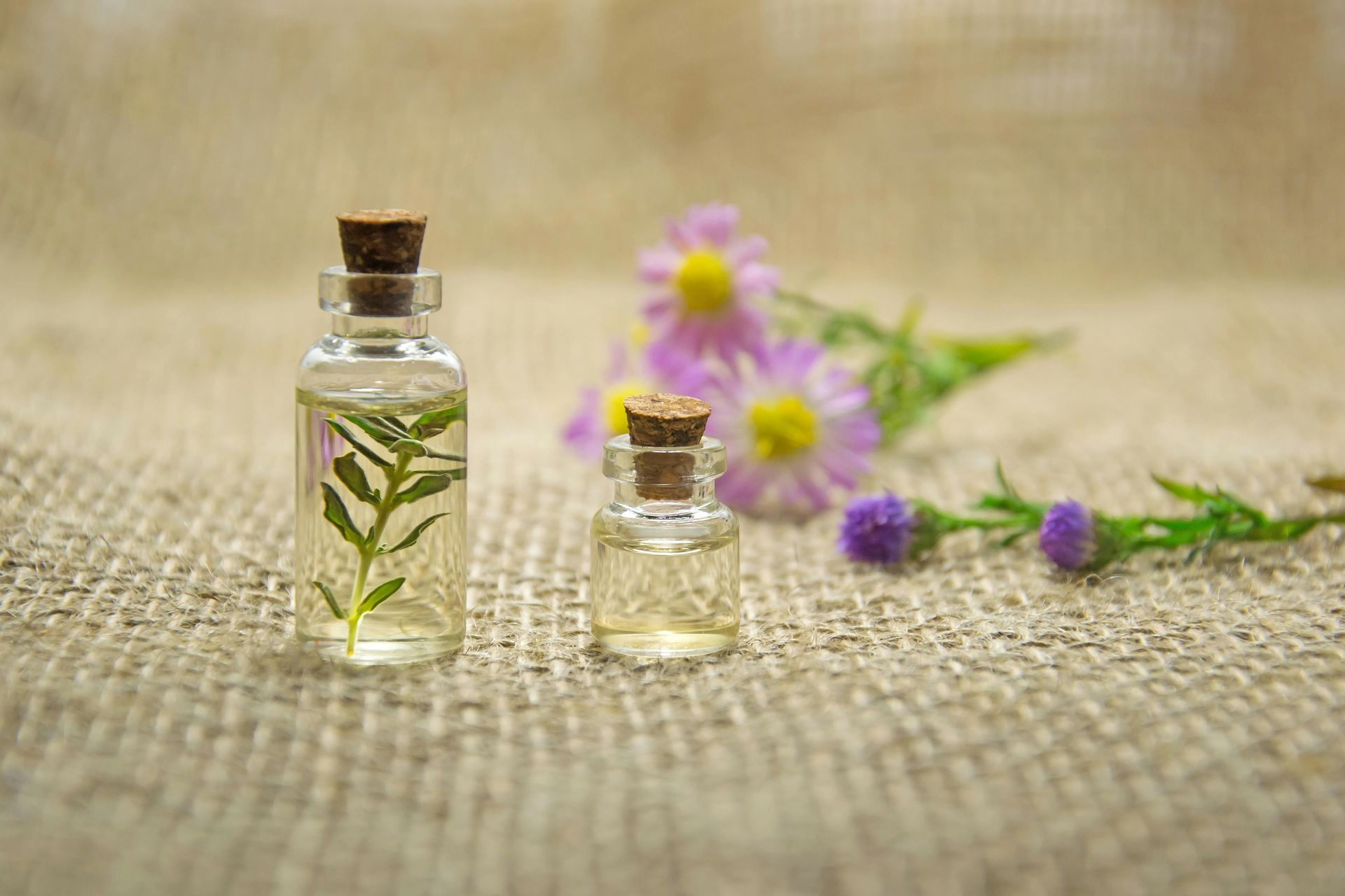 Two small bottles of essential oil with flowers in the background.