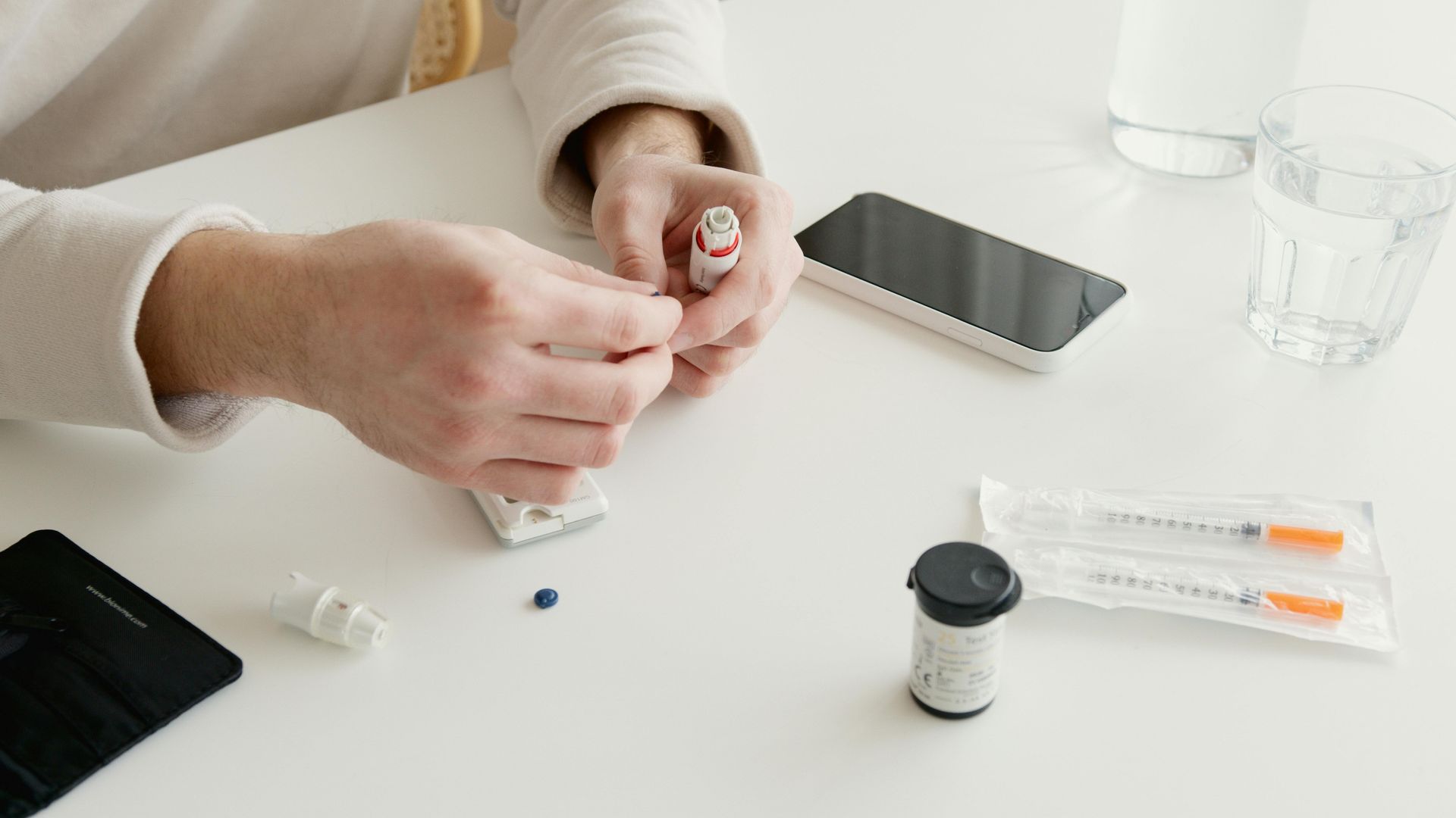 A person is sitting at a table with a cell phone and a bottle of pills.