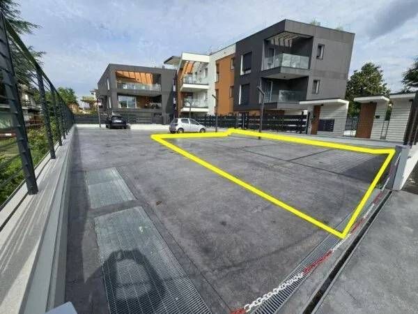 Parkplatz mit gelber Umrandung, die einen freien Platz hervorhebt; modernes Gebäude im Hintergrund.