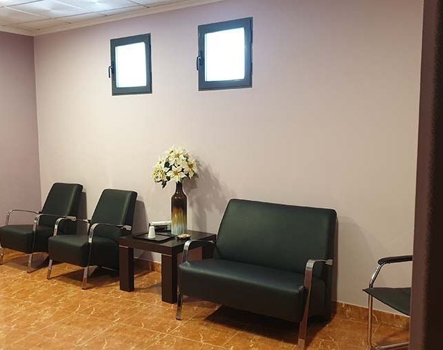 Una sala de espera con un sofá, sillas, mesas y un jarrón de flores.