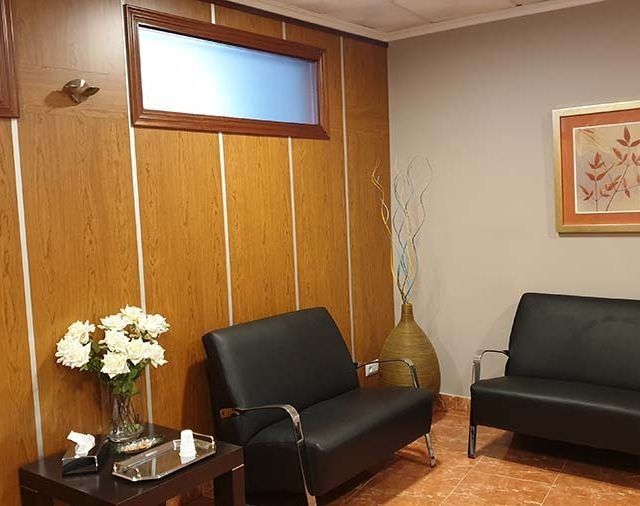 Una sala de espera con dos sillas negras y un jarrón de flores.