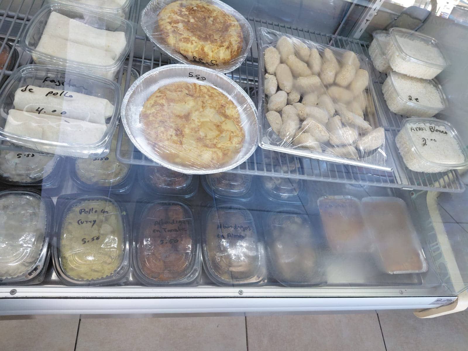 Vitrina con alimentos preparados: tortilla española, croquetas y otros platos en envases de plástico.