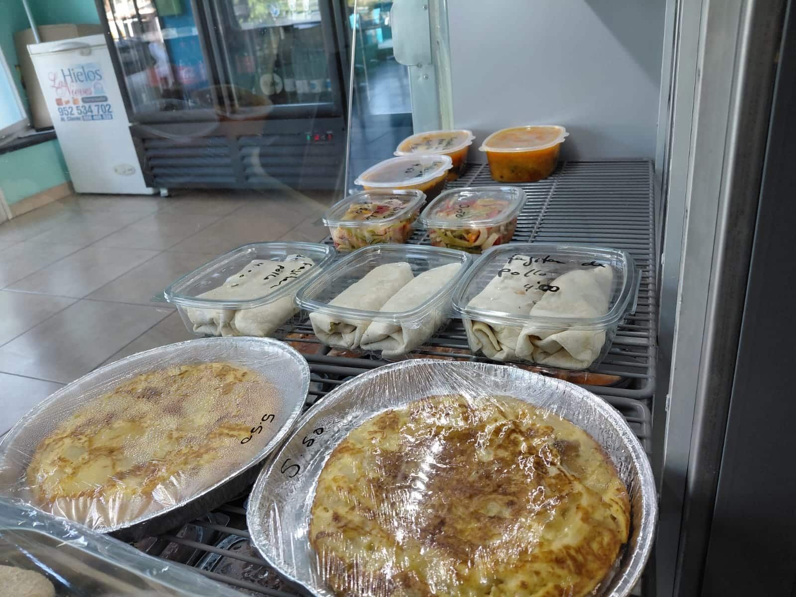 Alimentos preparados en recipientes de plástico transparente y latas de aluminio en un estante de una tienda.
