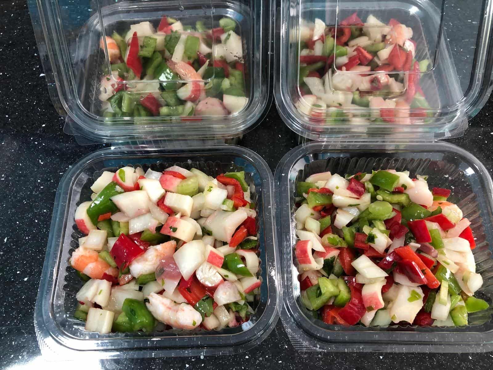 Cuatro recipientes de plástico llenos de una mezcla de ensalada de mariscos con camarones, pulpo y pimientos.
