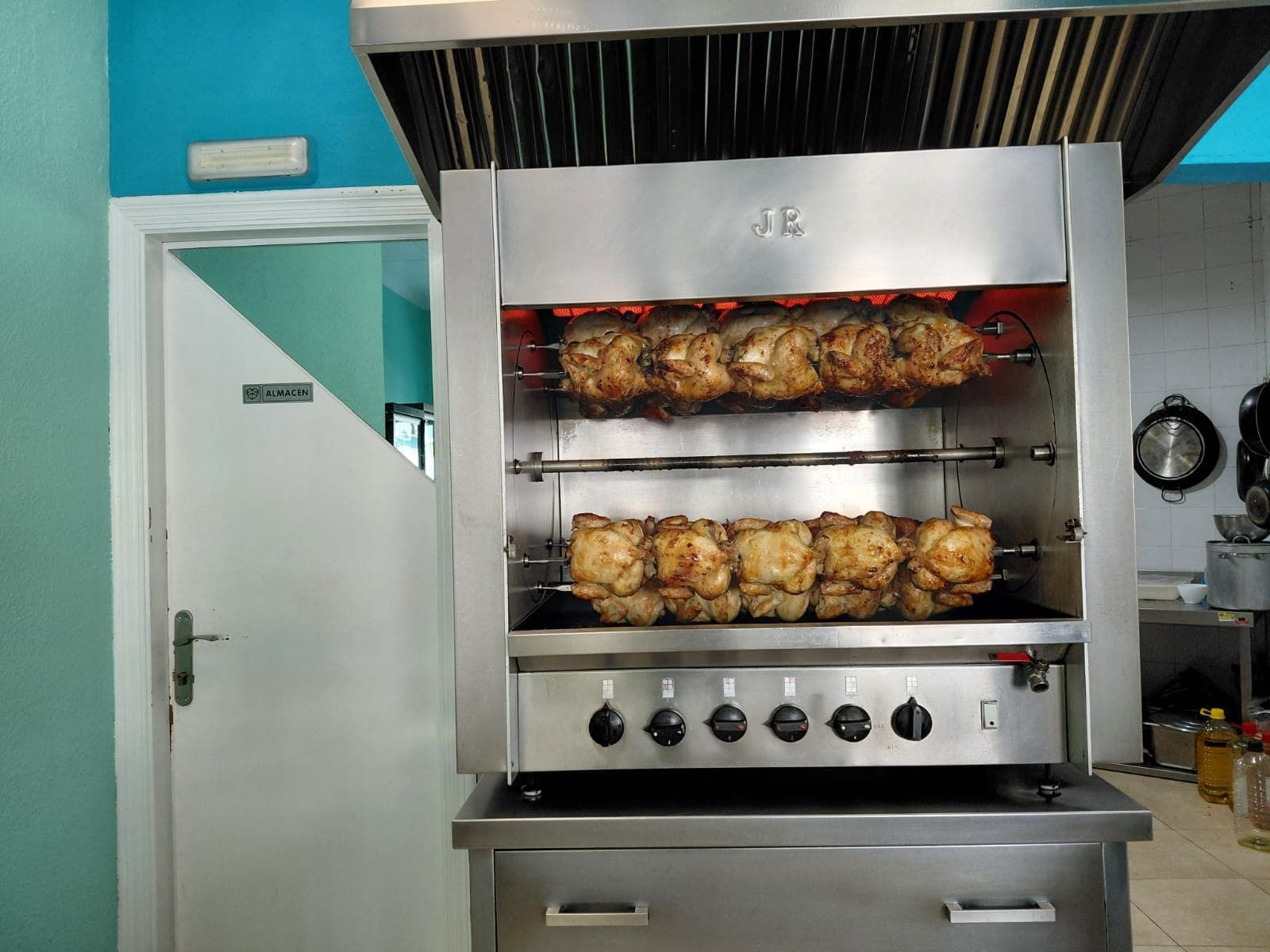 Un horno asador de acero inoxidable con pollos asándose en su interior, en una cocina.