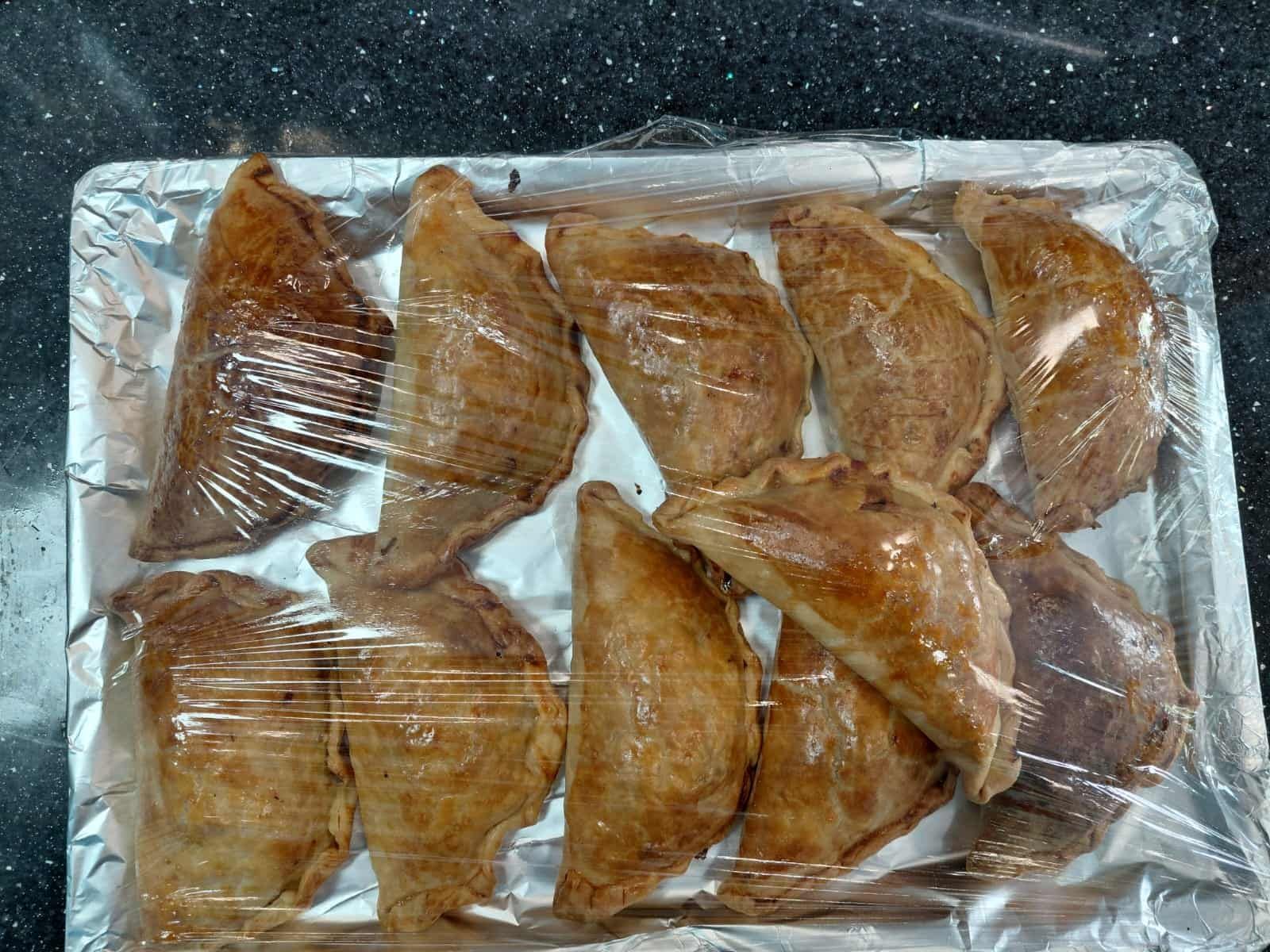 Bandeja de pasteles horneados de color marrón dorado envueltos en plástico sobre una bandeja forrada con papel de aluminio.