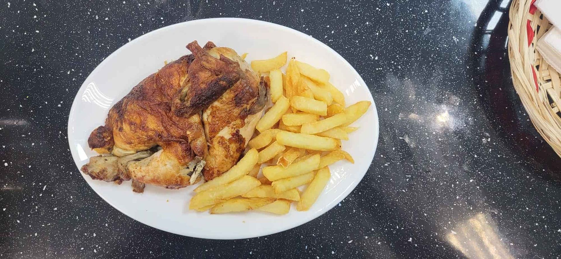 Plato de pollo asado y patatas fritas sobre una mesa moteada.