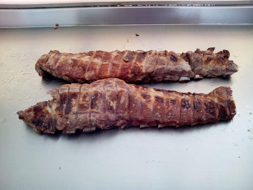Dos costillas de cerdo a la parrilla sobre una superficie de metal brillante.
