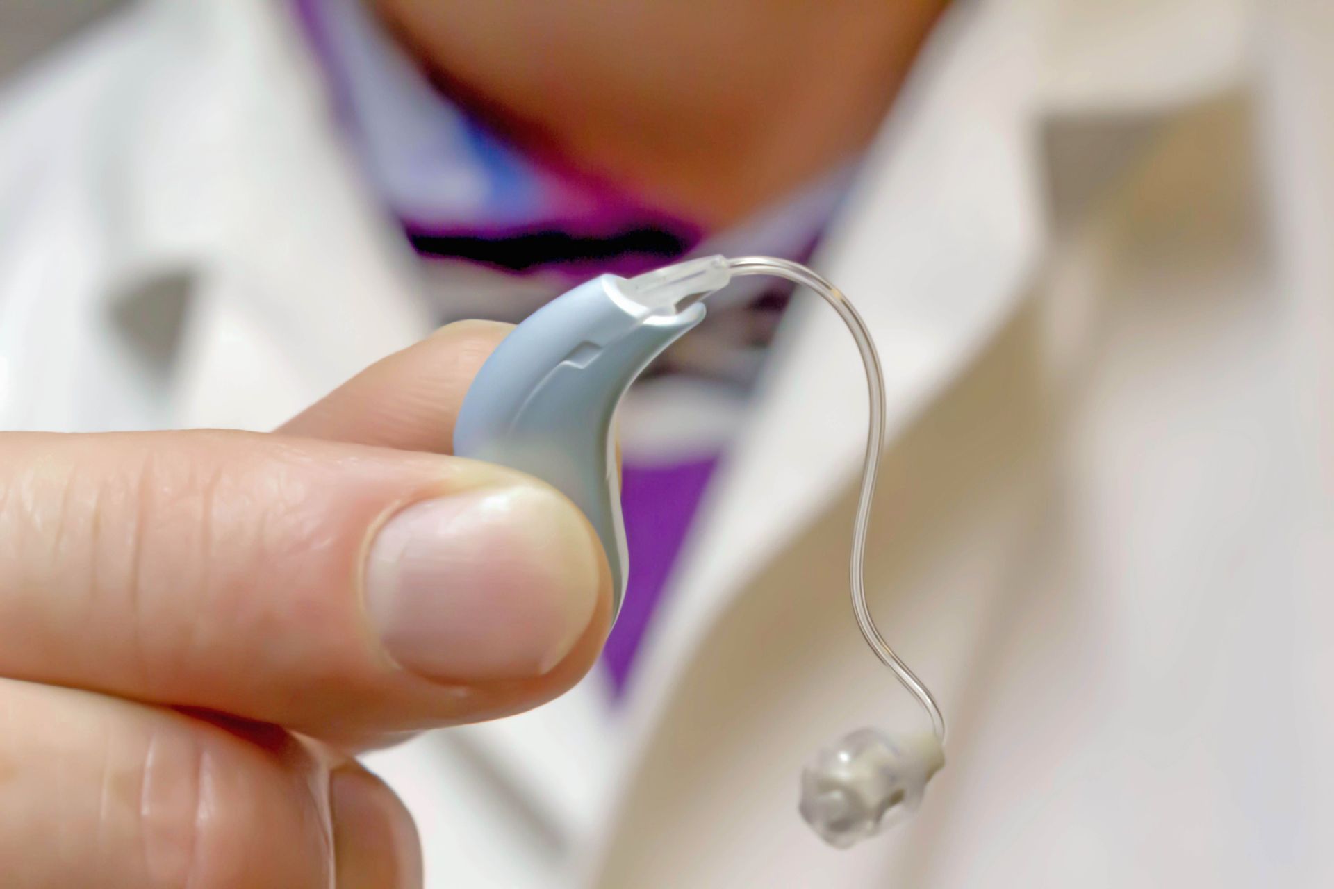 Mano sosteniendo un audífono azul claro con tubo transparente y almohadilla para el oído.