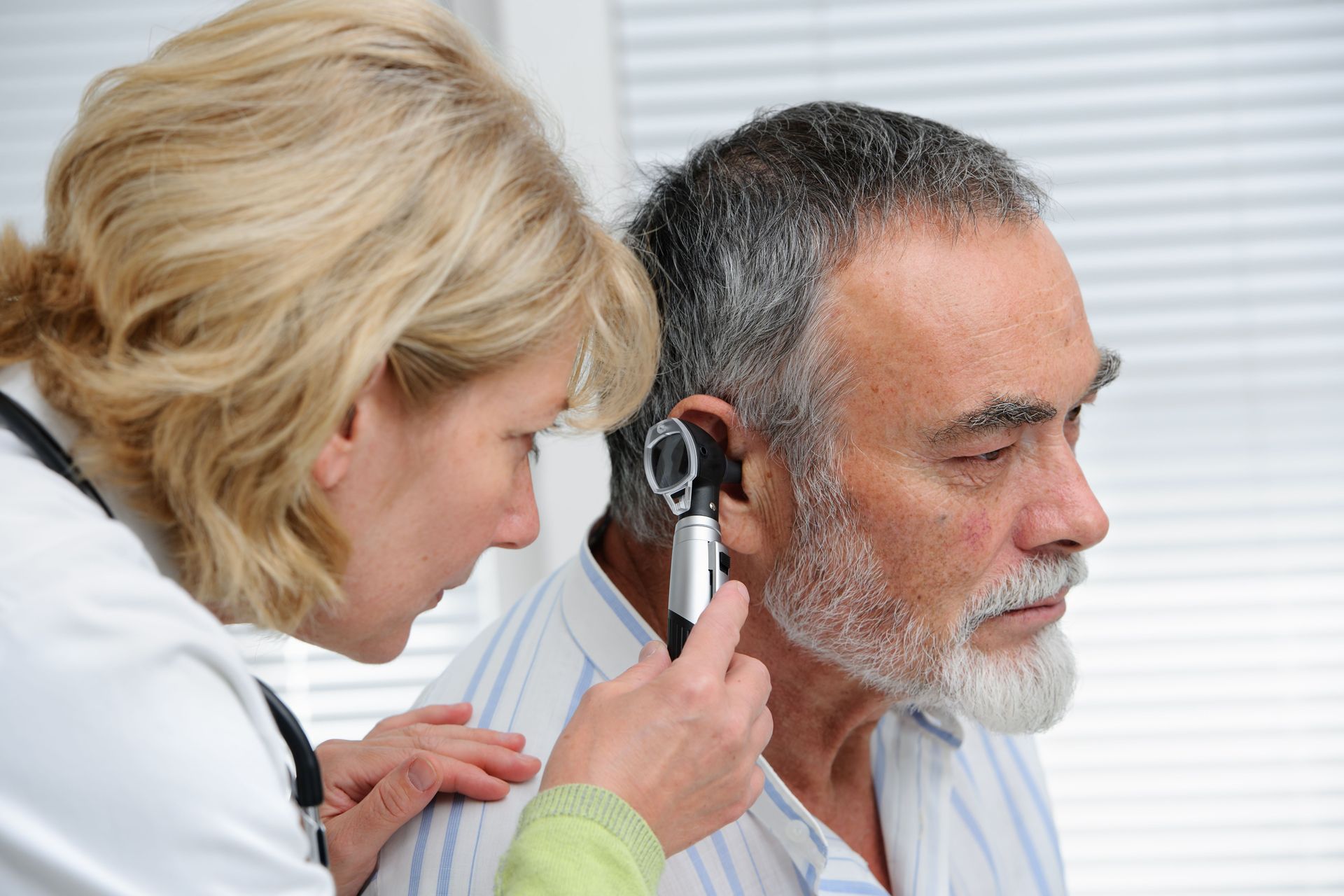 Médico examinando el oído de un paciente con un otoscopio en un consultorio médico.