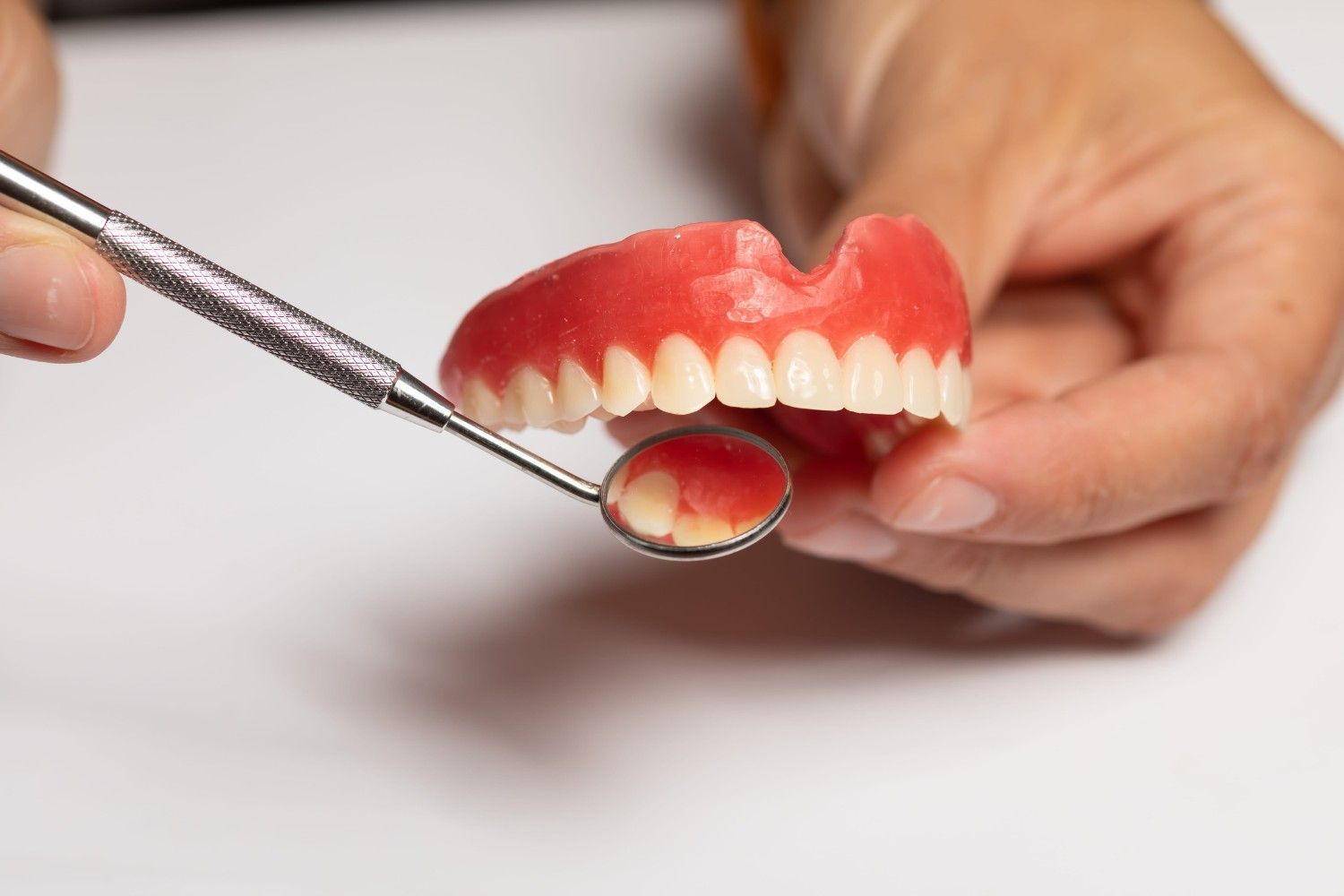 Unas manos sostienen un modelo dental mientras un espejo examina las encías y los dientes enrojecidos.