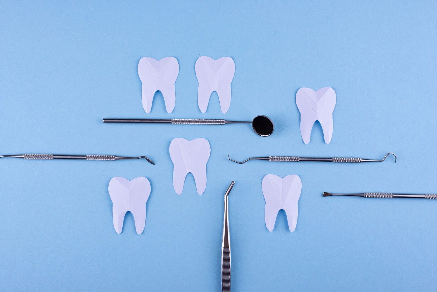 Instrumentos dentales y modelos con forma de diente sobre un fondo azul claro.