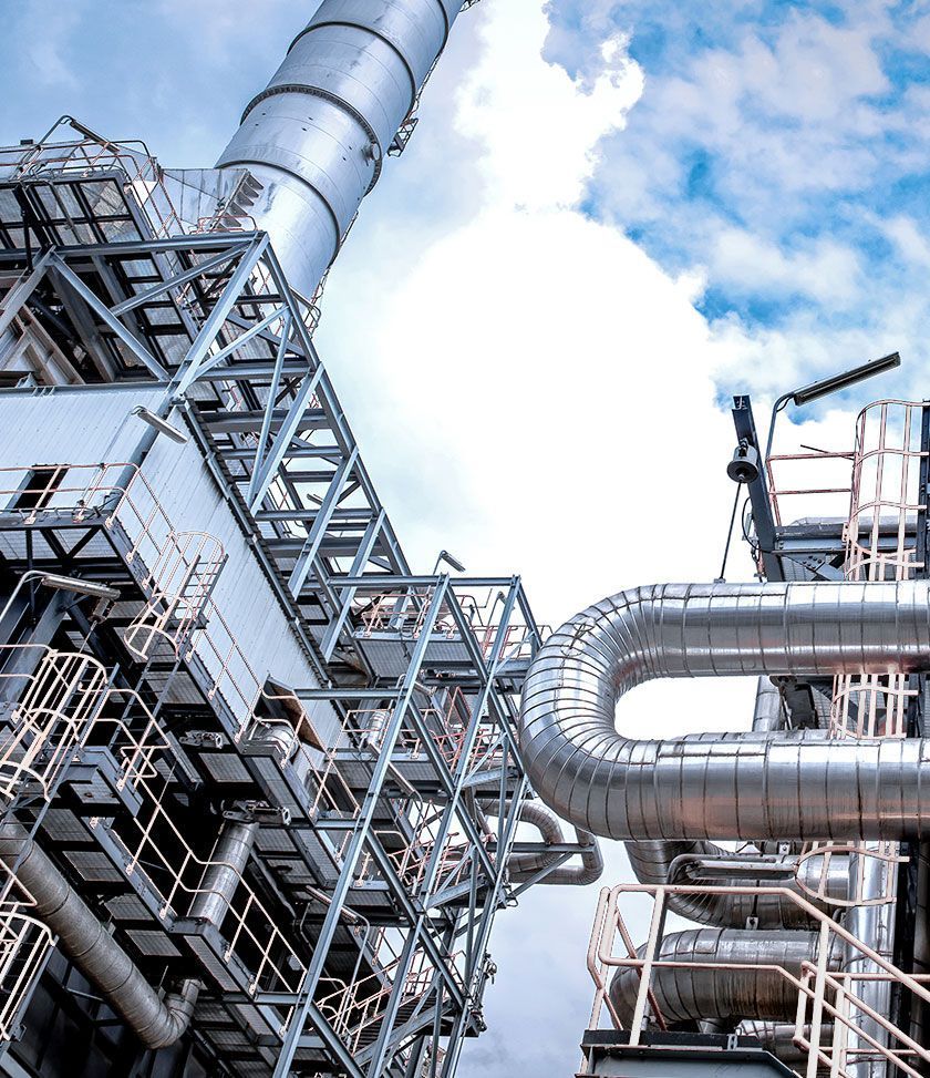 Industrielle Raffinerierohre und Metalltürme vor blauem Himmel mit Wolken