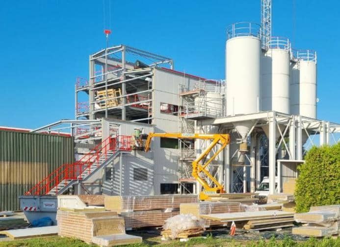 Industrieanlage mit Silos, Stahlgerüst und einem gelben Aufzug unter klarem, blauem Himmel