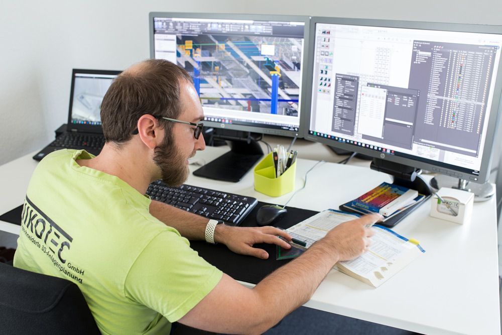 Eine Person arbeitet an einem Schreibtisch mit zwei Monitoren und benutzt Maus und Tastatur in einem hellen Büro.